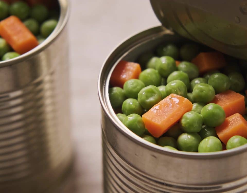 Boites de conserve ouvertes avec petits pois et carottes cuites dedans.