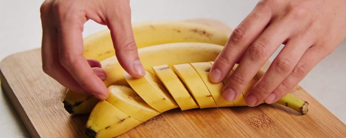 Mains préparant des bananes plantains jaunes sur planche.