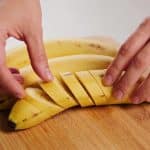 Mains préparant des bananes plantains jaunes sur planche.