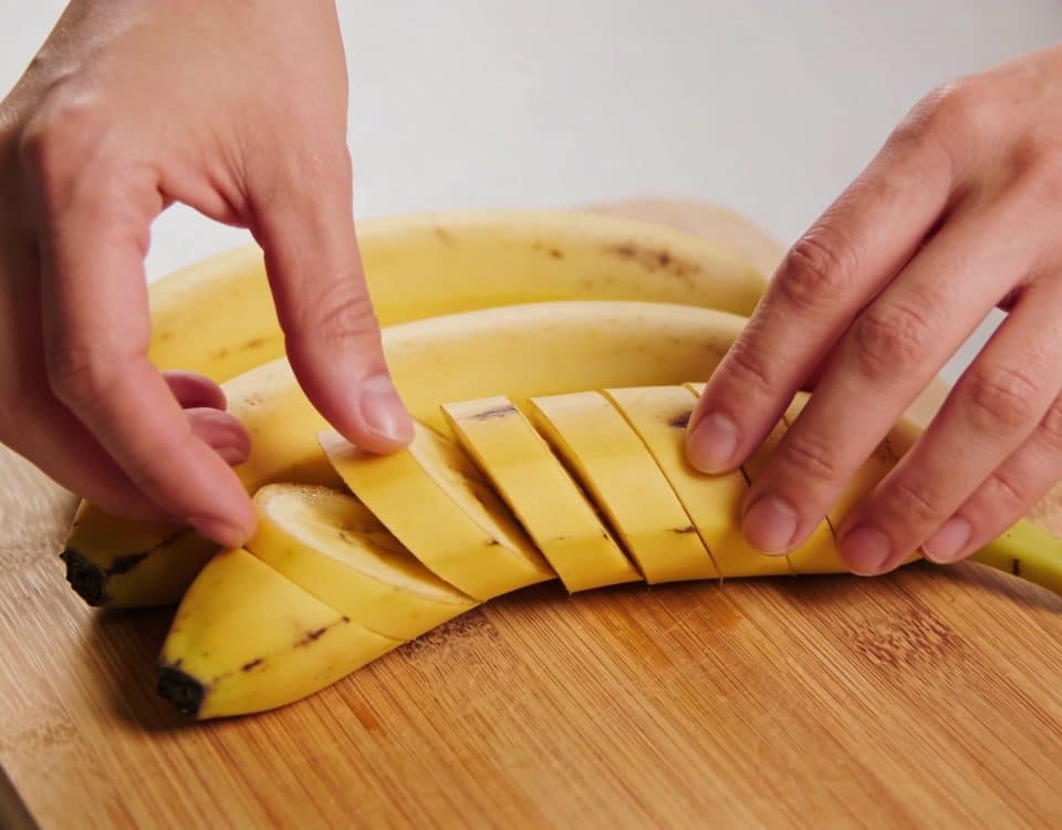 Mains préparant des bananes plantains jaunes sur planche.