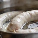 Mains versant du boudin blanc cru dans une casserole d'eau
